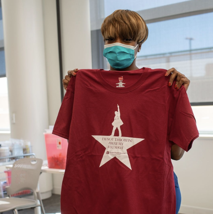 Health center nurse holding up giveaway flu shot T-shirt.